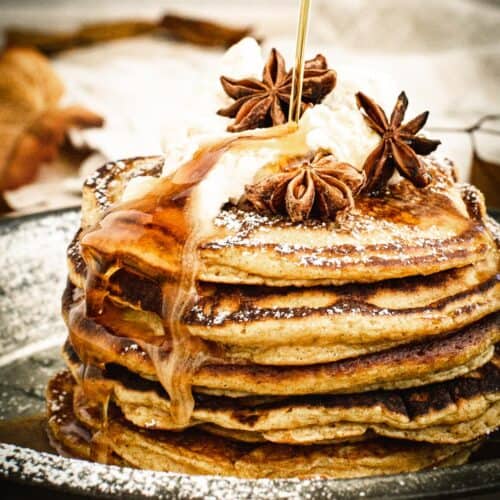 Drizzling syrup on top of pumpkin pancakes with whipped cream and powdered sugar.