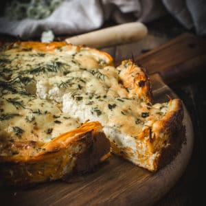 goat cheese and herb quiche with slice cut out on wooden board