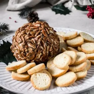 pecan covered cheese ball on white plate with bread crostini