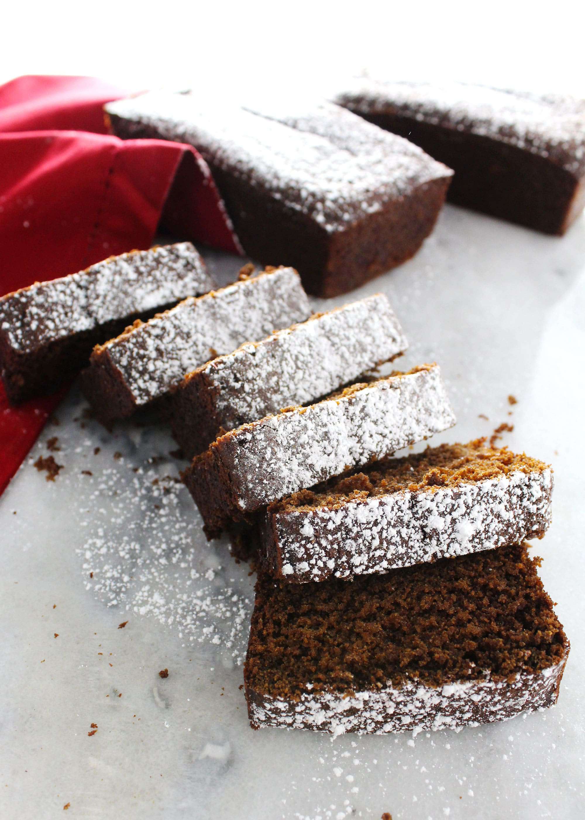 gingerbread loaf sliced and dusted with powdered sugar on a red napkin