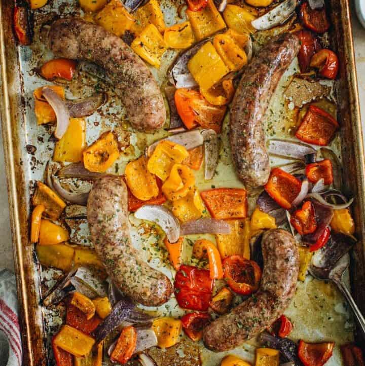 Sausage and peppers in the oven on a rimmed baking sheet.