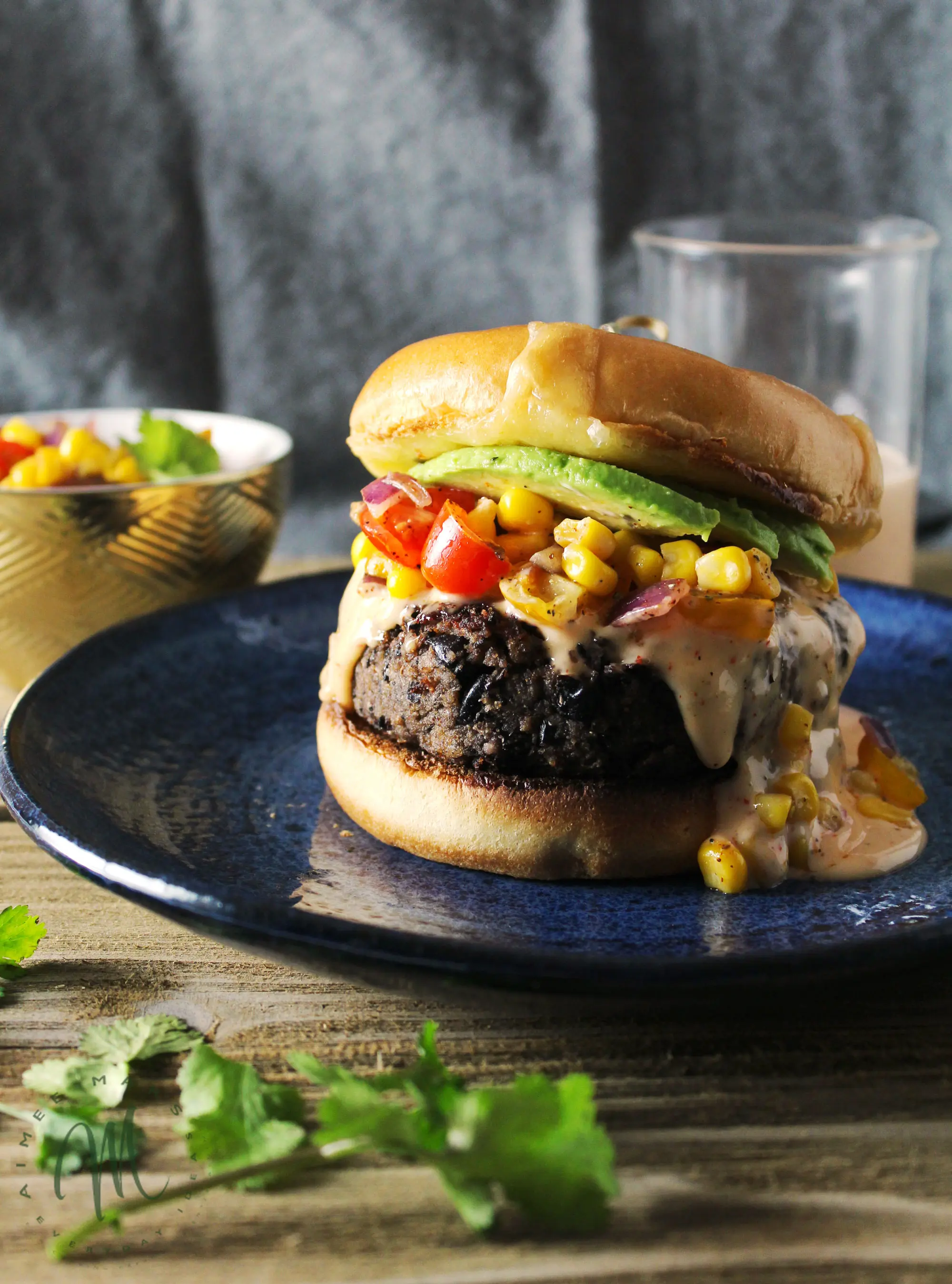 Southwest black bean burger topped with corn salsa and an avocado on a blue plate.