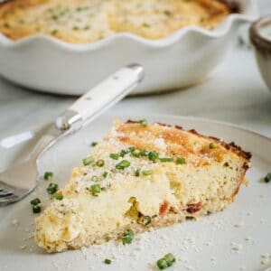 Cauliflower crust quiche slice topped with chives and grated cheese on white plate.