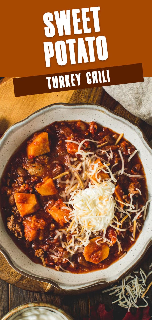 Sweet potato turkey chili topped with cheese and sour cream in a pottery bowl.