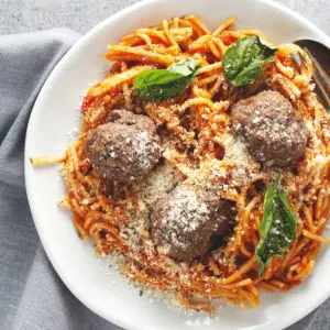 Spaghetti and meatballs with basil on top on a white plate.