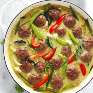 Meatballs in a green curry sauce in a large white skillet.