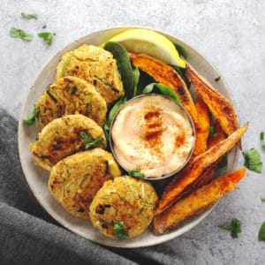 Chickpea zucchini fritters on a round plate with sweet potato wedges.