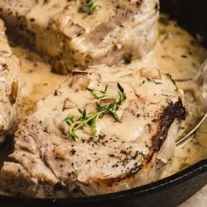 Apple Cider Brined Pork Chops in a creamy apple cider sauce in an iron skillet.