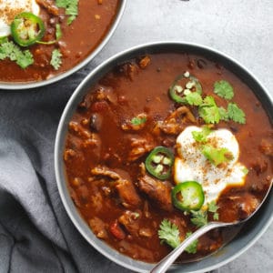 Pumpkin beef chili in gray bowls topped with sour cream.