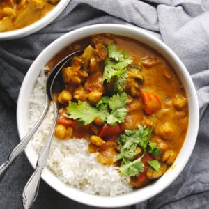 Vegetable tikka masala over rice in a white bowl with silverware.