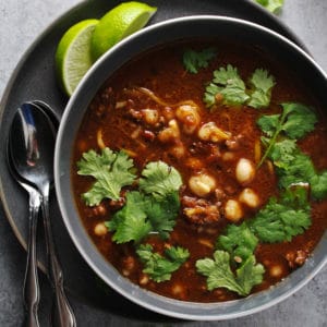 Beef pozole rojo in a black bowl topped with cilantro.