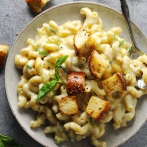 Hidden zucchini mac and cheese topped with homemade croutons on a gray plate.