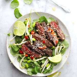 Korean BBQ steak salad with lime wedges on the side on a round plate.