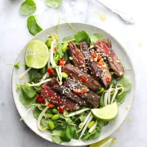 Korean BBQ steak salad with lime wedges on the side on a round plate.