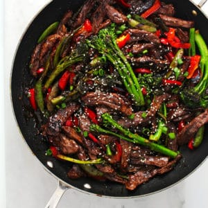 Beef stir fry tossed with vegetables in a large black skillet and topped with sesame seeds.