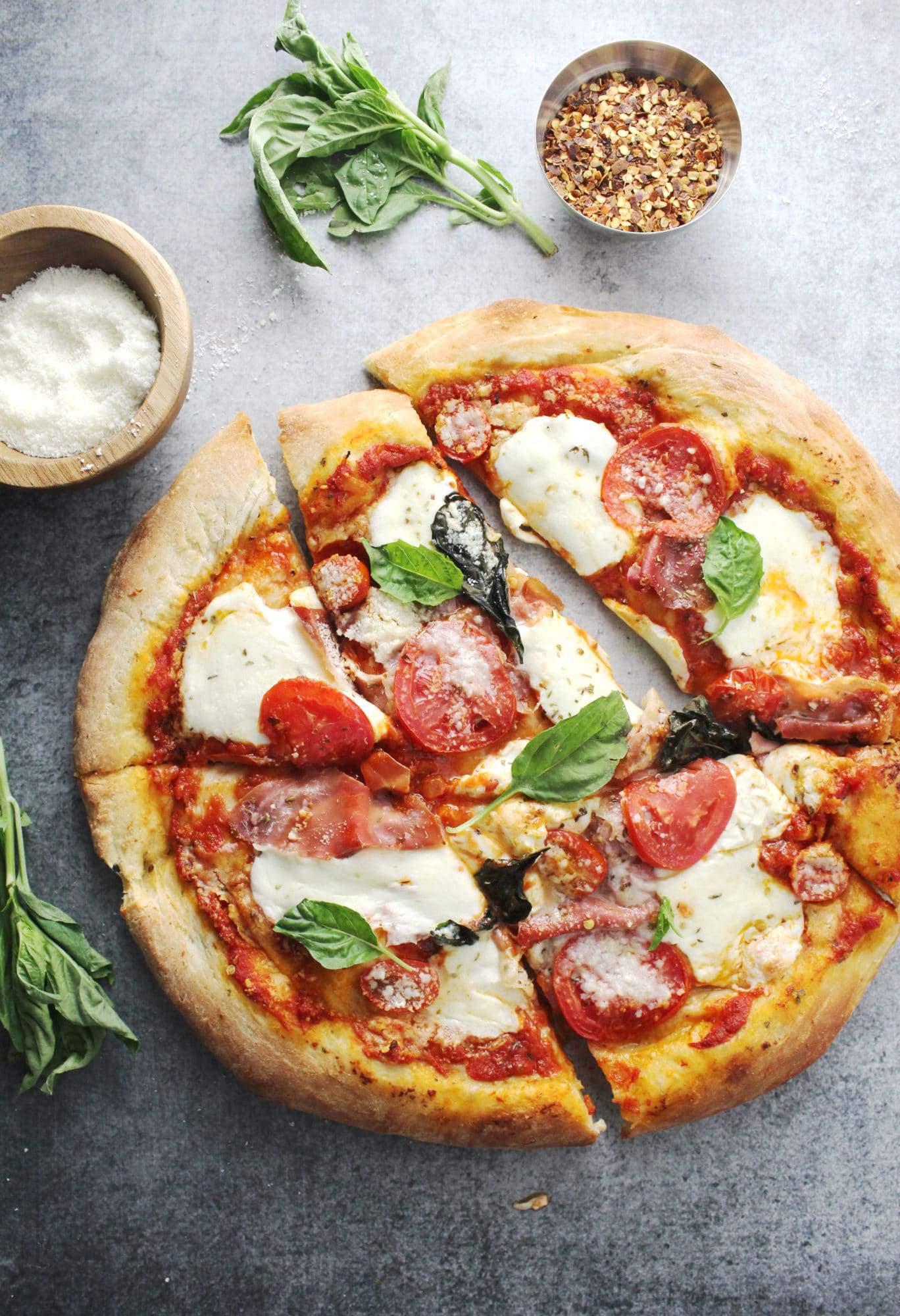 mozzarella pizza sliced on gray background with grated cheese in wooden bowl