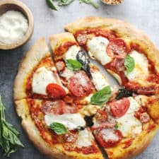 mozzarella pizza sliced on gray background with grated cheese in wooden bowl