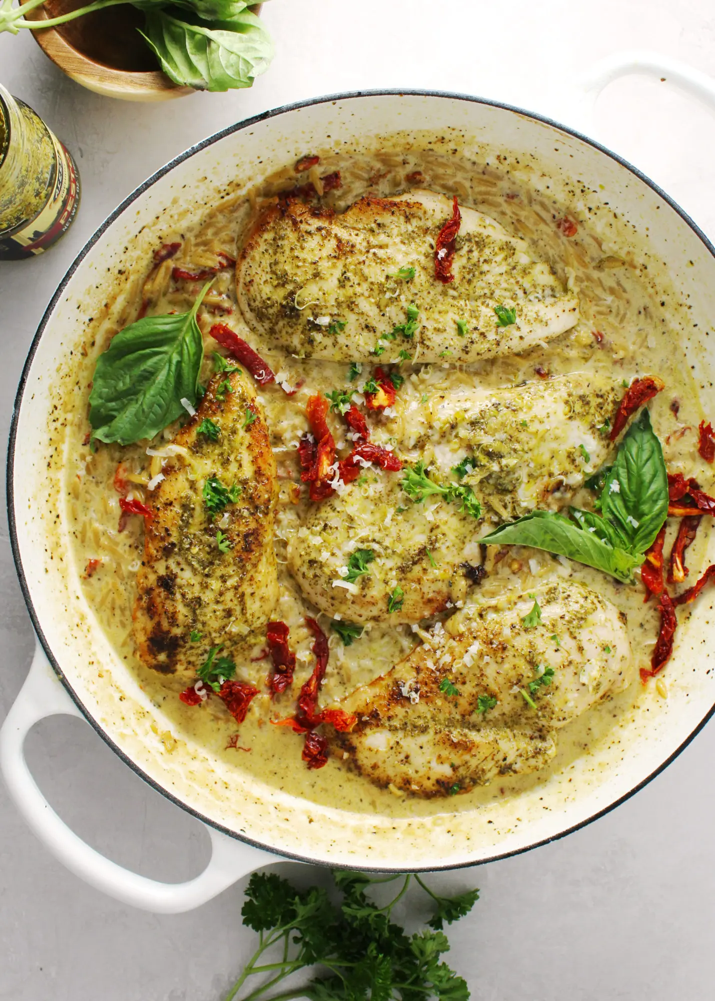 Creamy basil pesto chicken topped with fresh basil leaves in a white skillet.