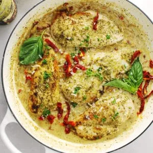 Creamy basil pesto chicken in a white skillet.