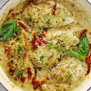 Creamy Basil Pesto Chicken topped with sun-dried tomatoes and basil leaf.