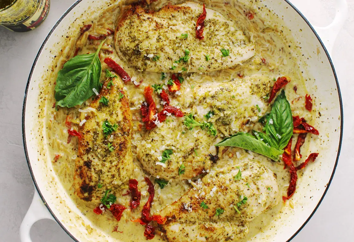 Creamy Basil Pesto Chicken topped with sun-dried tomatoes and basil leaf.