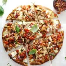 Bruschetta pizza topped with chicken and basil leave on a white surface.