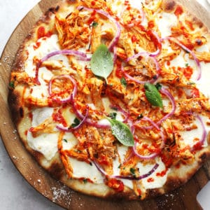 Buffalo chicken pizza topped with fresh basil on a round wooden board.