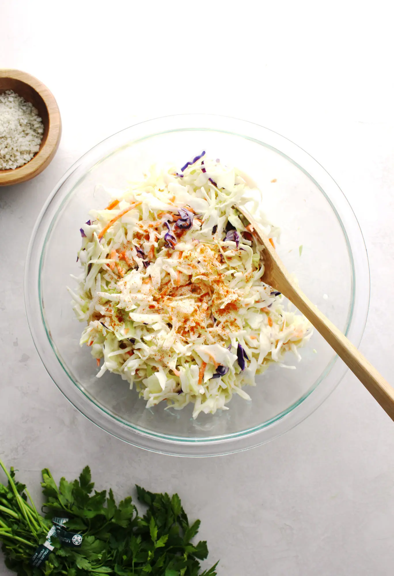 coleslaw in a clear glass bowl with wooden spoon