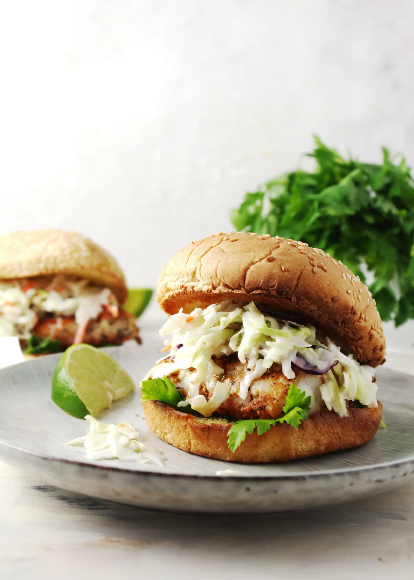 Close up of fish sandwich on a gray plate with lime wedge on the side.