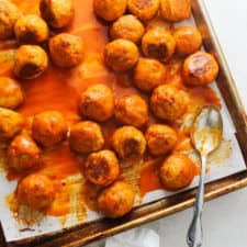 Buffalo Chicken Meatballs on a rimmed baking sheet with a silver spoon covered in sauce.