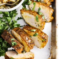 Pineapple turmeric glazed pork tenderloin sliced on a baking sheet with a bowl of cabbage.