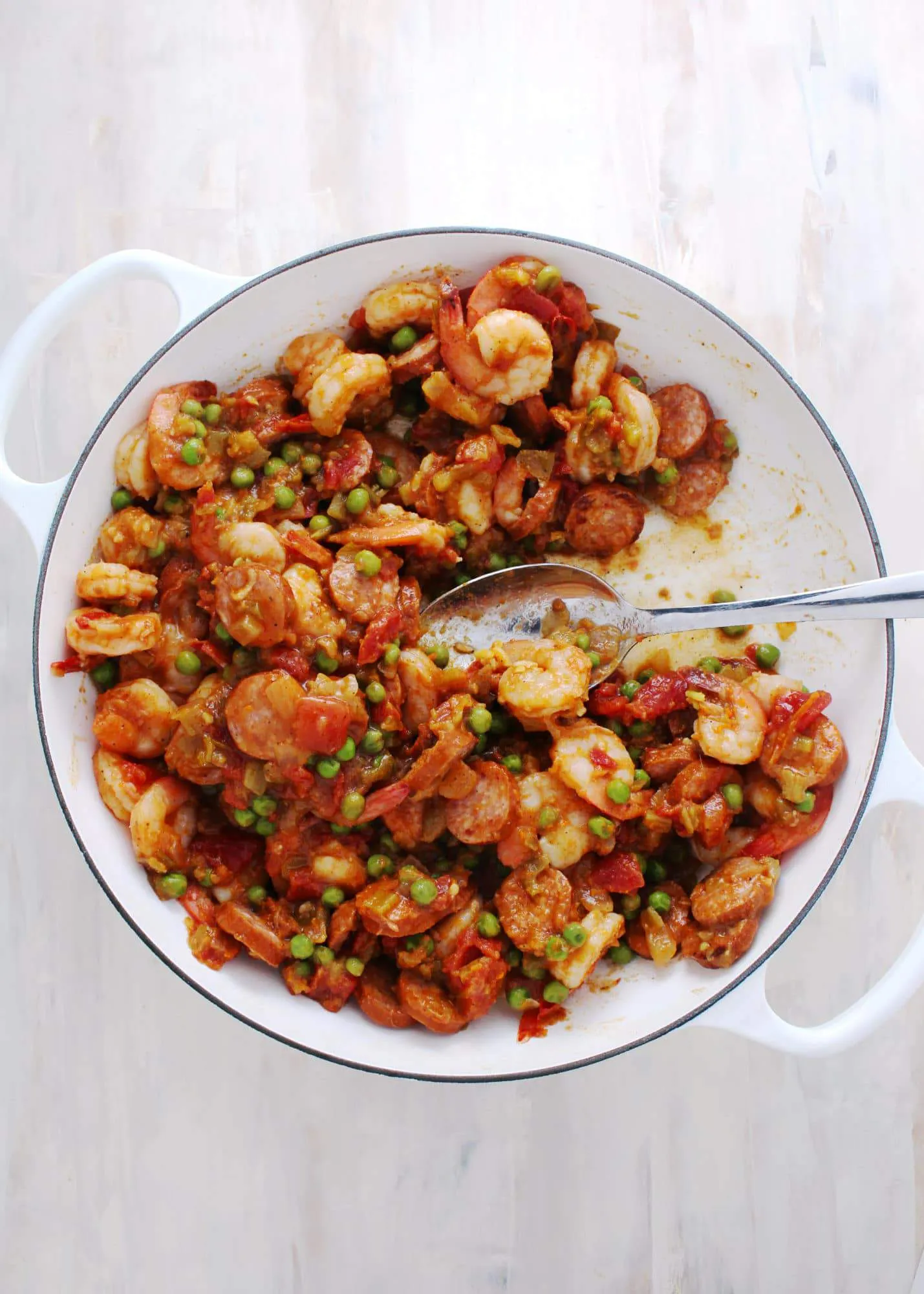 shrimp vegetables and sausage mix in a white skillet with silver spoon