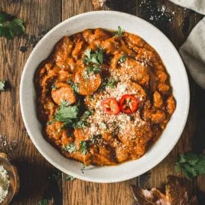 Sausage and pumpkin chili topped with cheese and cilantro in a white bowl.