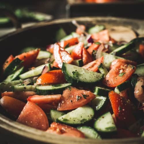 Italian cucumber, onion, and tomato salad in a large wooden bowl.