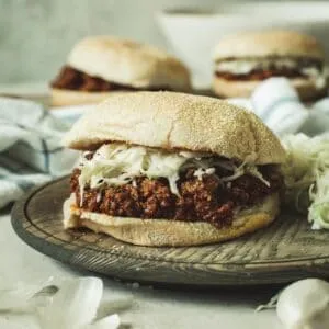 Sloppy Joe topped with coleslaw sitting on a wooden plate.