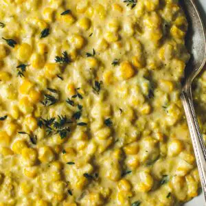 Creamed corn with fresh thyme on top and a silver serving spoon.