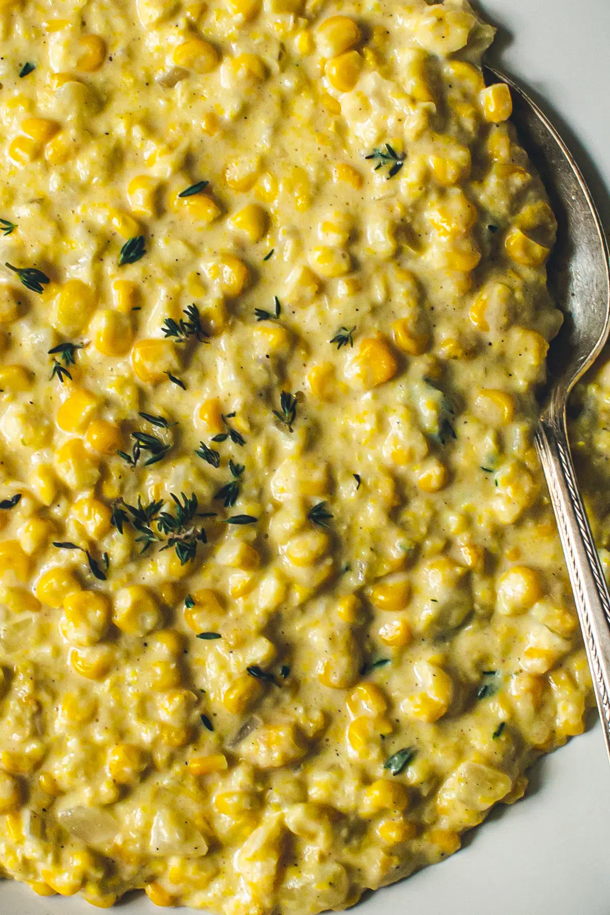 Creamed corn with fresh thyme on top and a silver serving spoon.