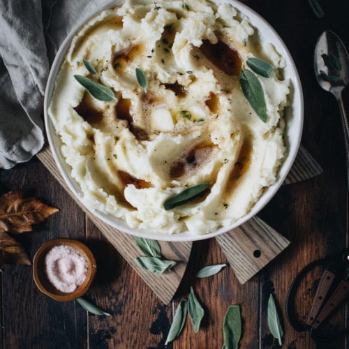 Brown butter garlic mashed potatoes in a bowl sitting on a cutting board.