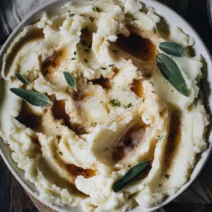 Brown butter mashed potatoes in a large bowl topped with fresh sage.