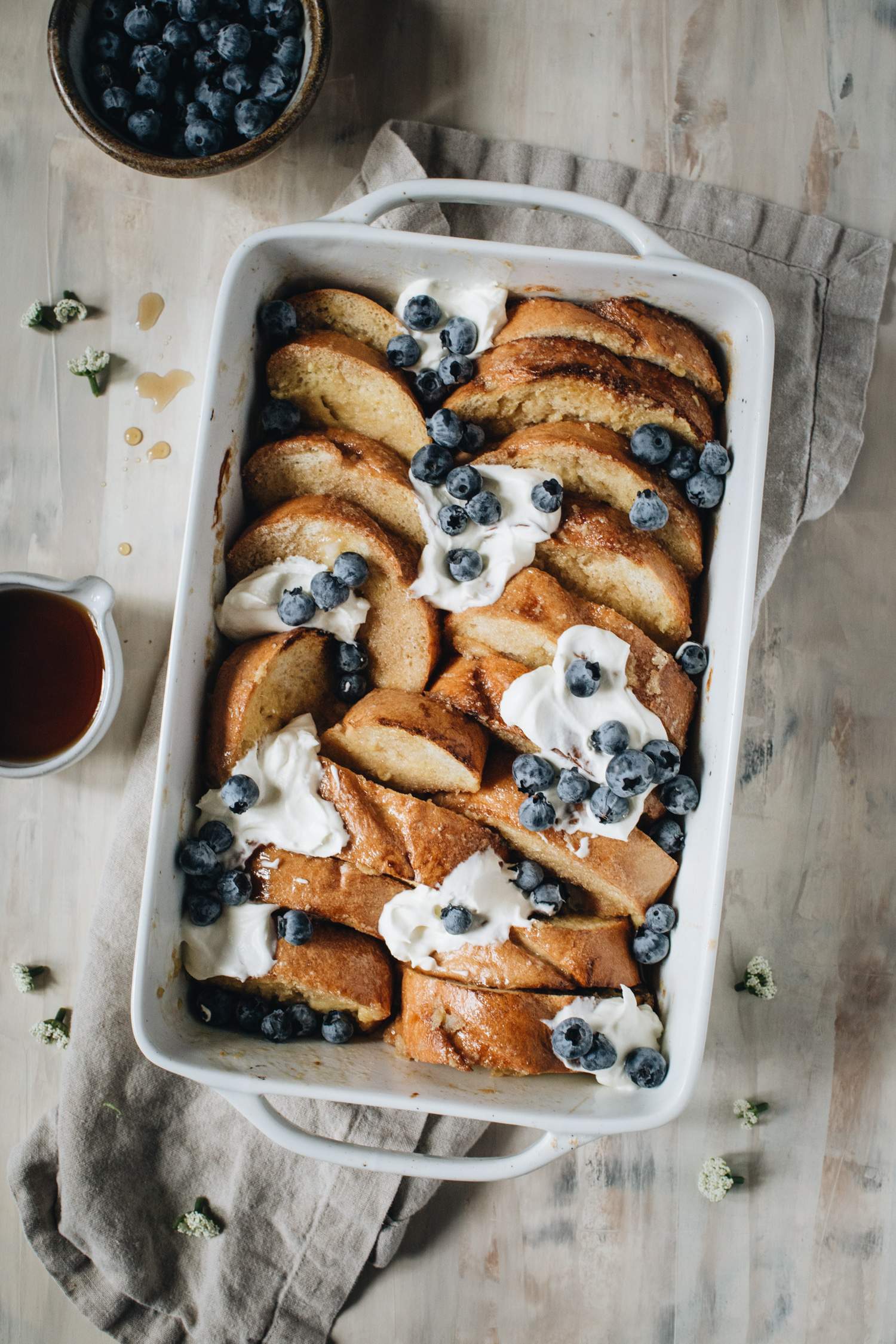 creme brulee french toast in white casserole dish with whipped cream and blueberries