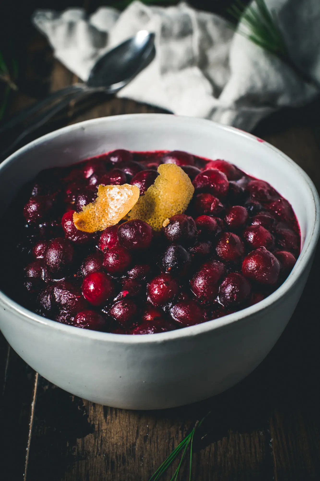 cranberry sauce in white bowl with spoon and orange peel topping