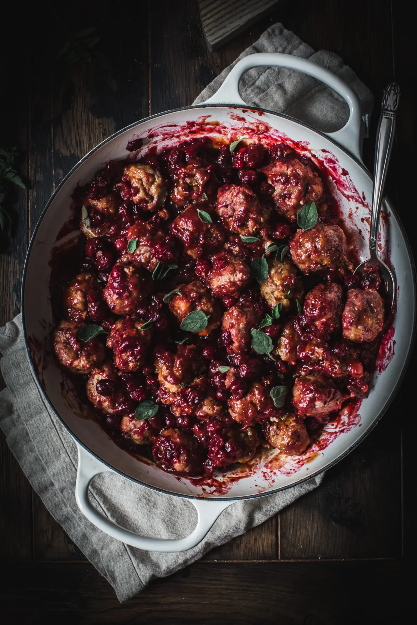 cranberry meatballs in white skillet on wooden table with silver spoon