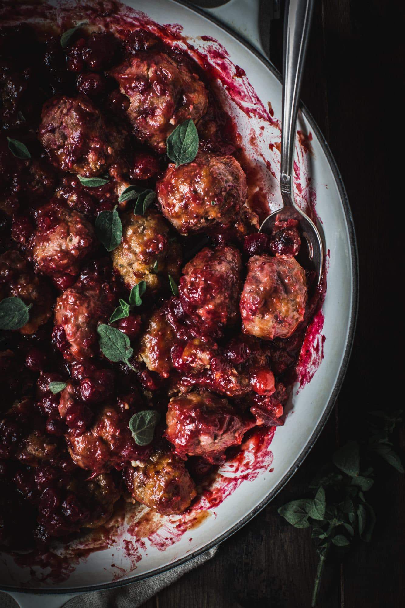 close up of cranberry meatballs with fresh oregano and silver spoon