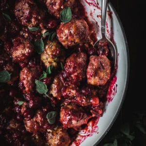 close up of cranberry meatballs with fresh oregano and silver spoon