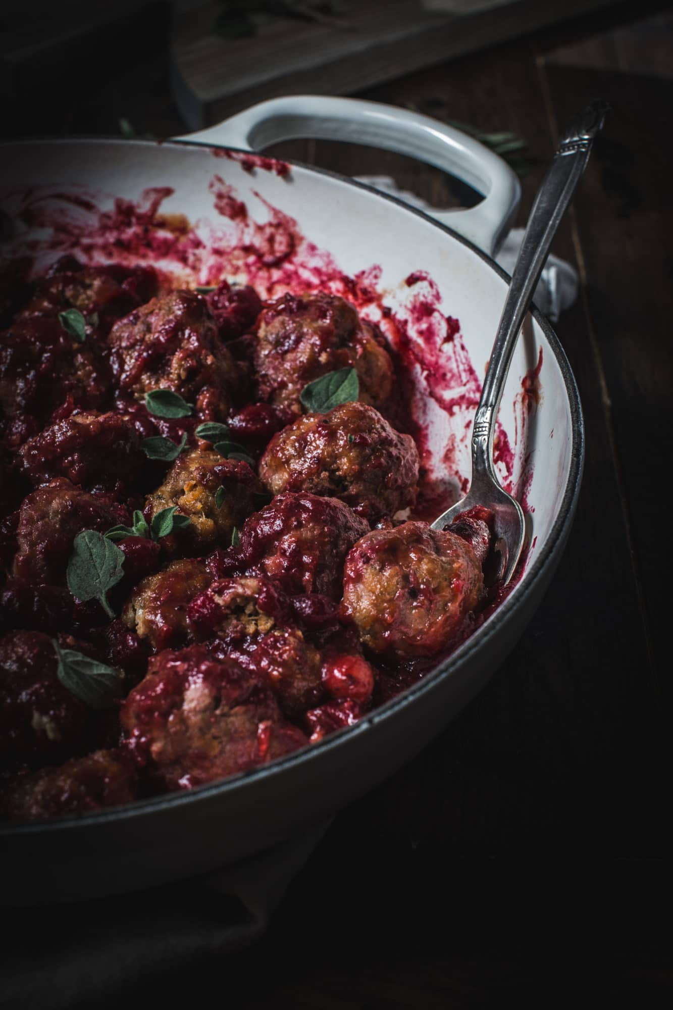 close up of cranberry meatballs with fresh oregano and silver spoon
