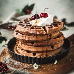 waffles stacked with whipped cream, cherries and pouring syrup