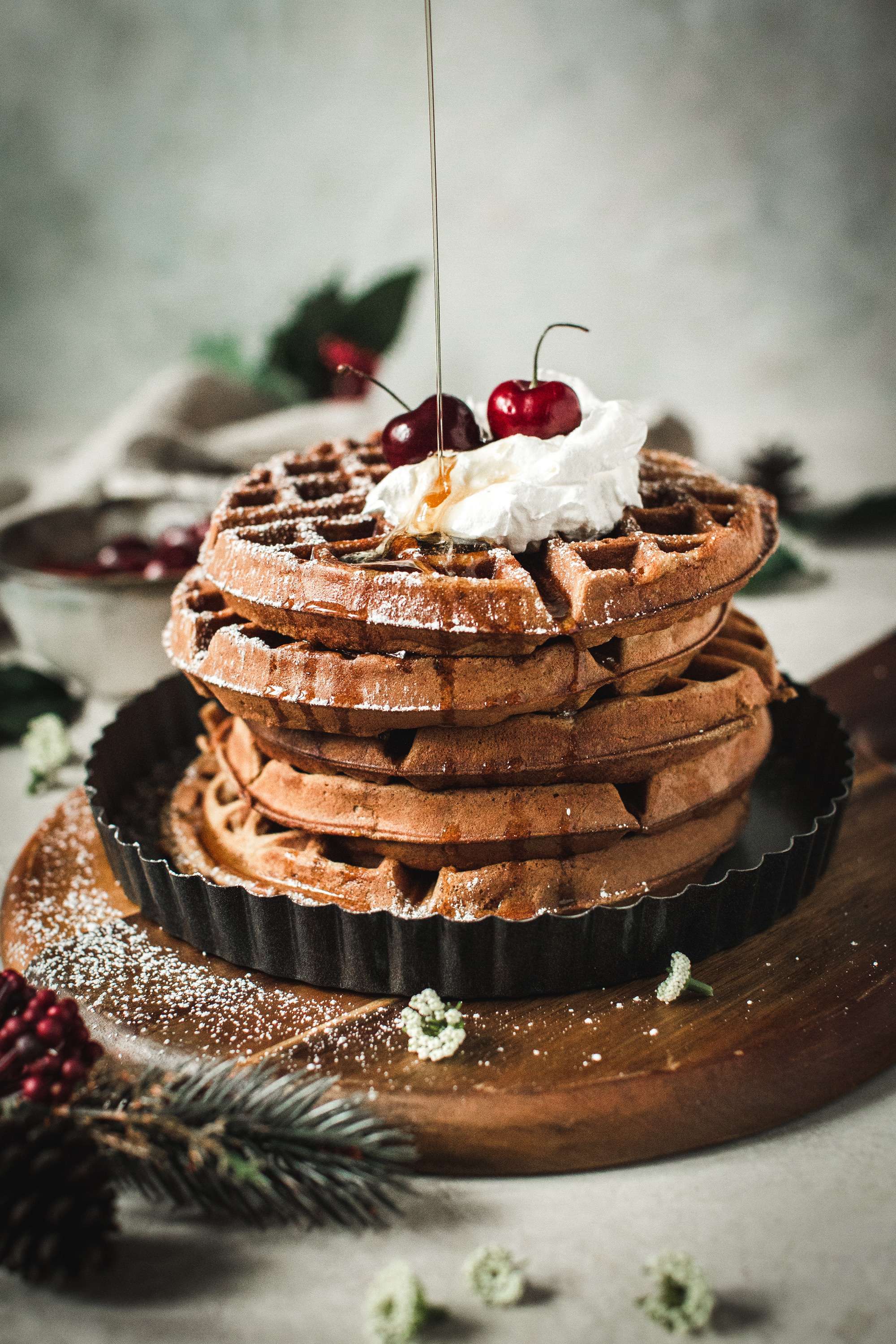 waffles stacked with whipped cream, cherries and pouring syrup