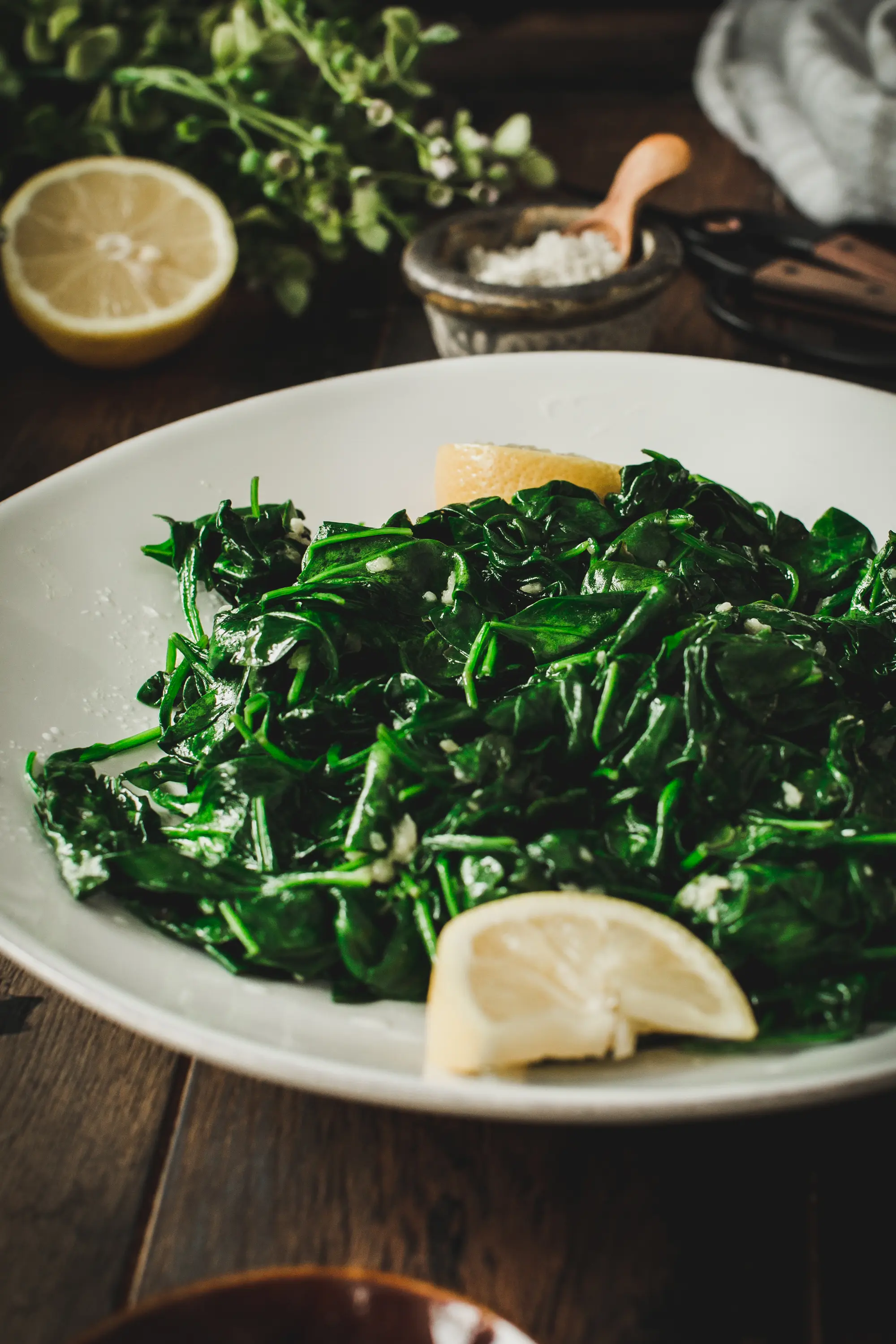 wilted garlic lemon spinach on white dish with lemon wedges