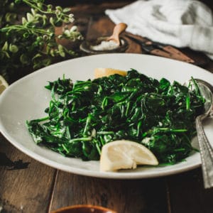 Sautéed spinach on a white plate with lemon wedge.