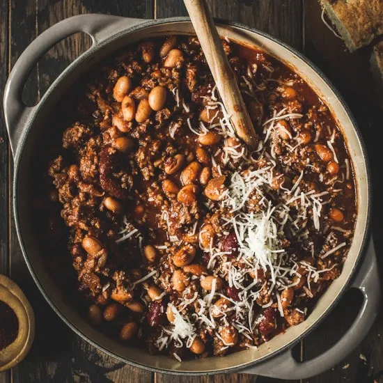 ground beef and bean chili in gray dutch oven topped with shredded cheese